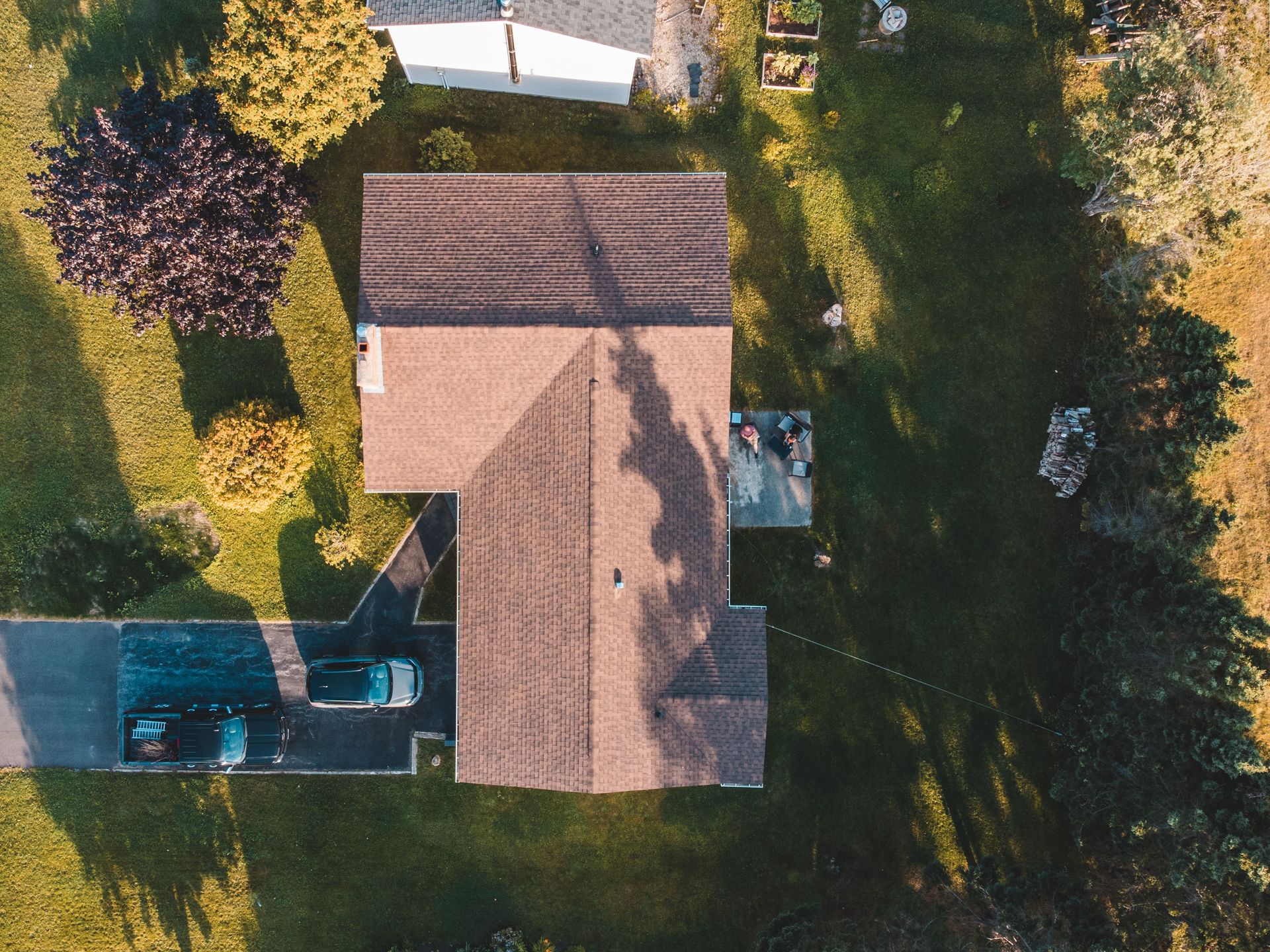 Drone shot capturing a suburban house with parked cars and a green lawn.