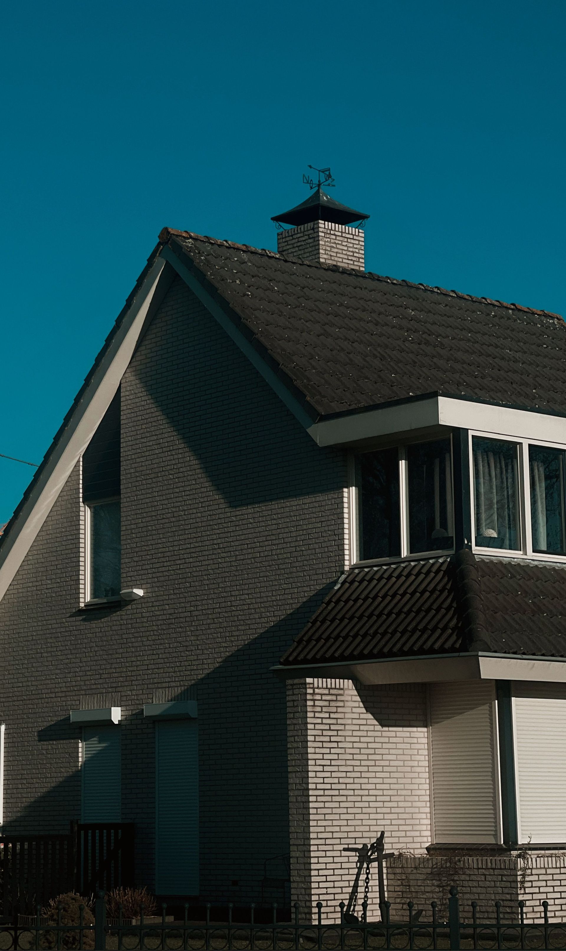 Sunlit modern suburban house with steep roof and chimney under a clear blue sky.